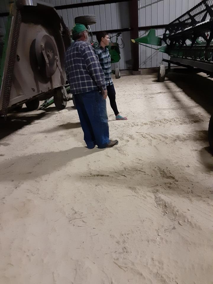 Zeph and Mat admiring a corn harvesting head with miscellaneous farm equipment in the background