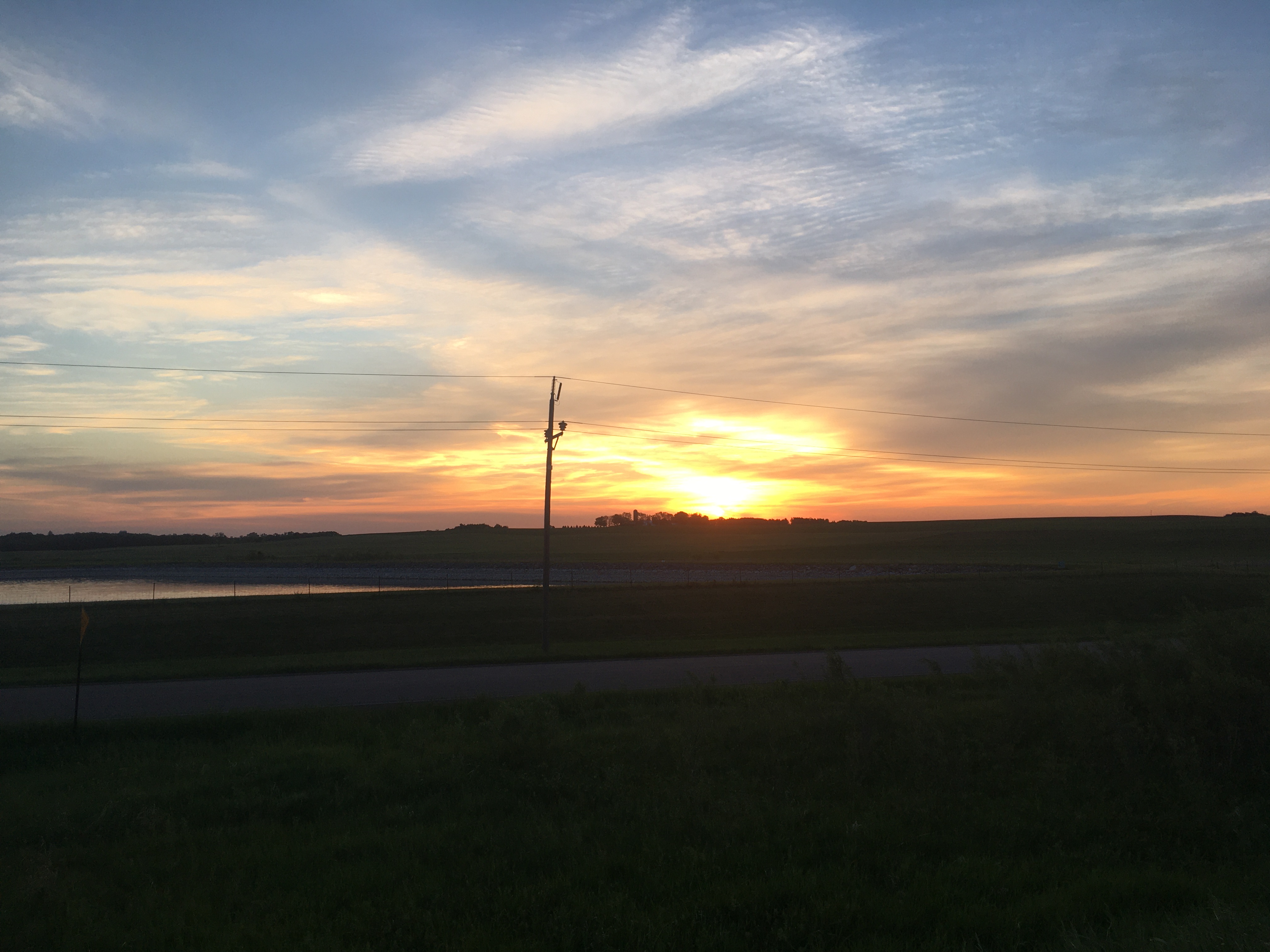 A brilliant yellow and orange
sunset with some wispy/ripply clouds, and the silhouette of some trees and
a power pole in the foreground. A river is also visible by the way it
reflects the sunset.