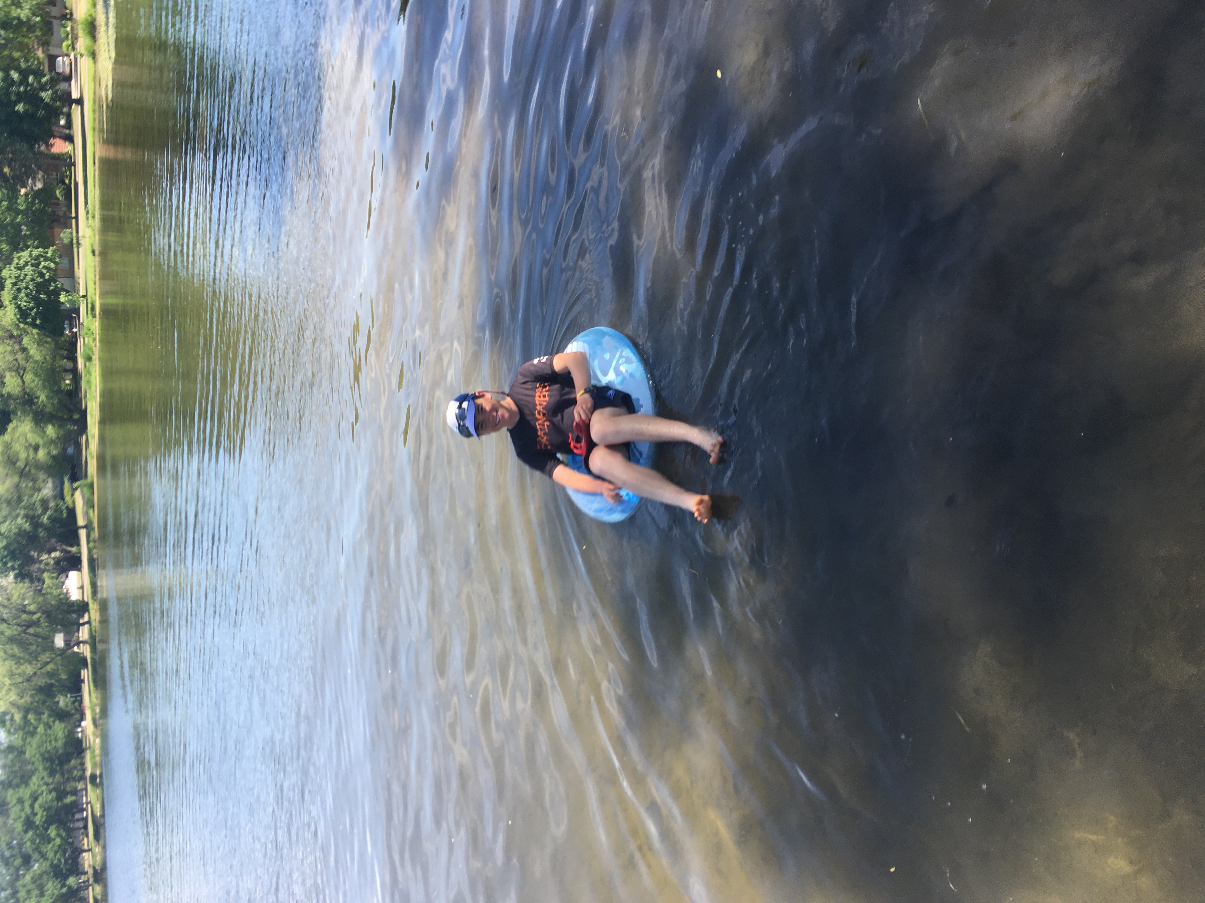 Zeph floats in a blue inner
tube in a calm lake, partially shaded by trees on shore.