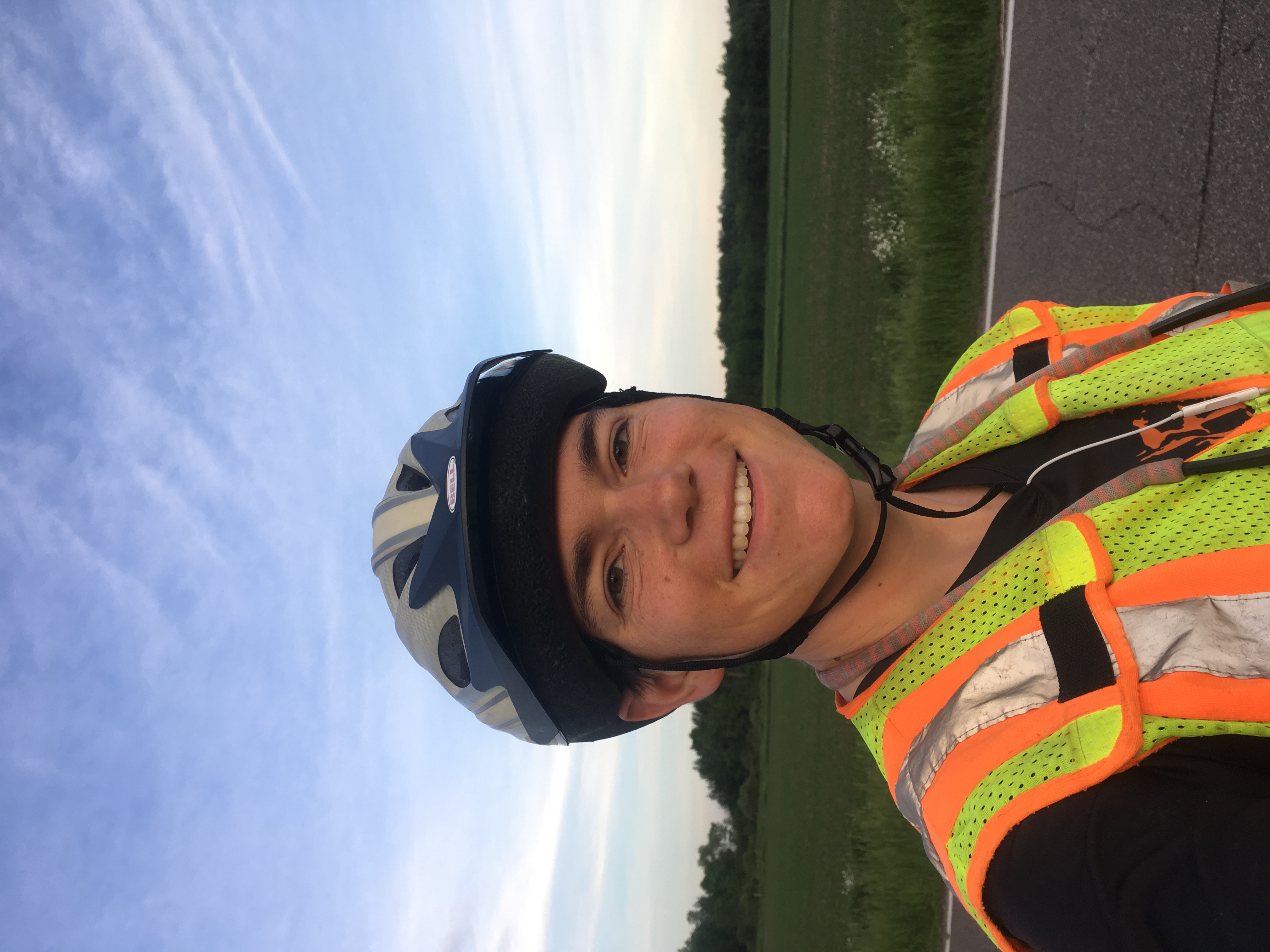 Zeph in reflective vest, helmet, and short sleeves smiling at the camera with early morning sky behind