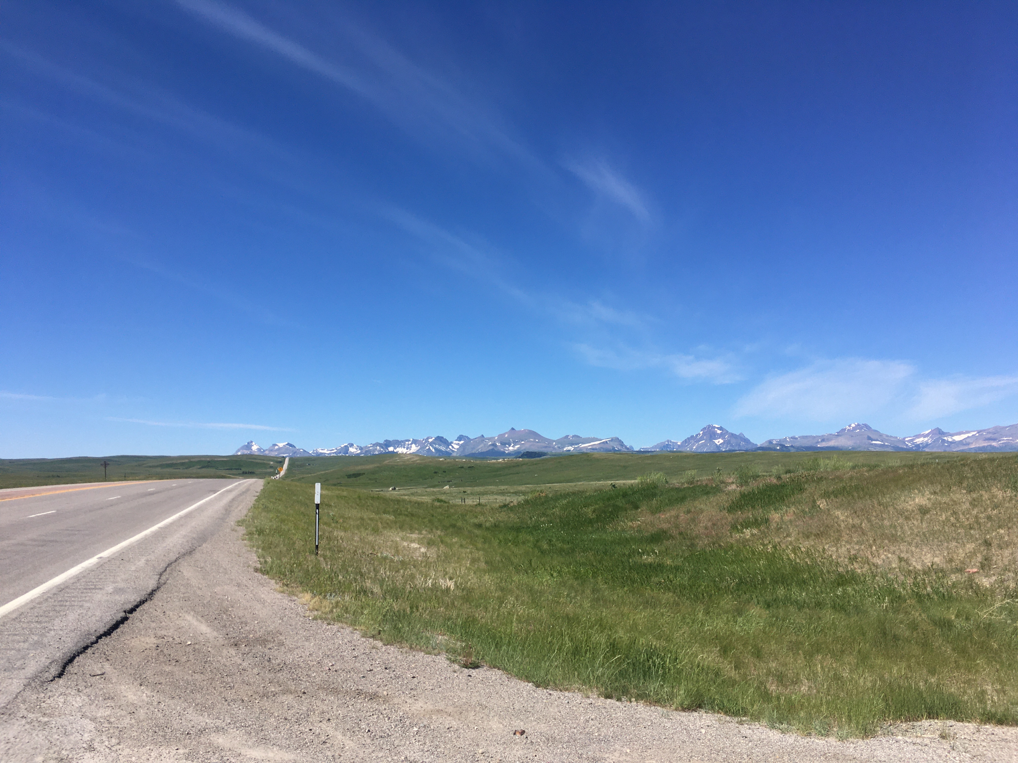 A four-lane highway fades into
the distance, with grassy fields beyond and to the side. There are no trees
in sight. In the distance are just quintessential mountains, with some snow
in shaded patches but mostly bare, and a glorious blue sky with just the
lightest wisp of cloud.