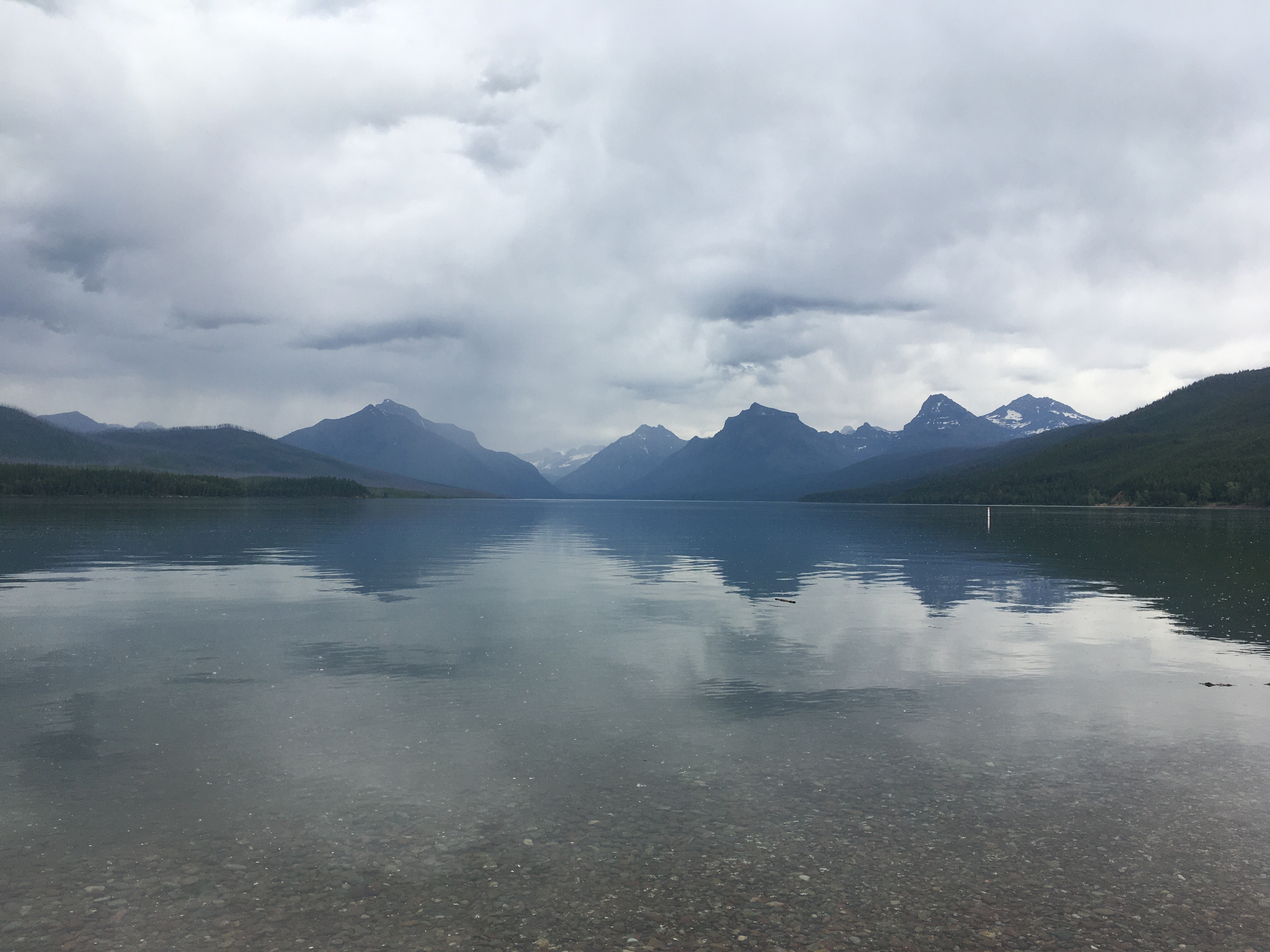 Mountains in the distance are
reflected in a mostly-calm lake. In the foreground some rocks are visible
under the surface. The sky is filled with puffy clouds.