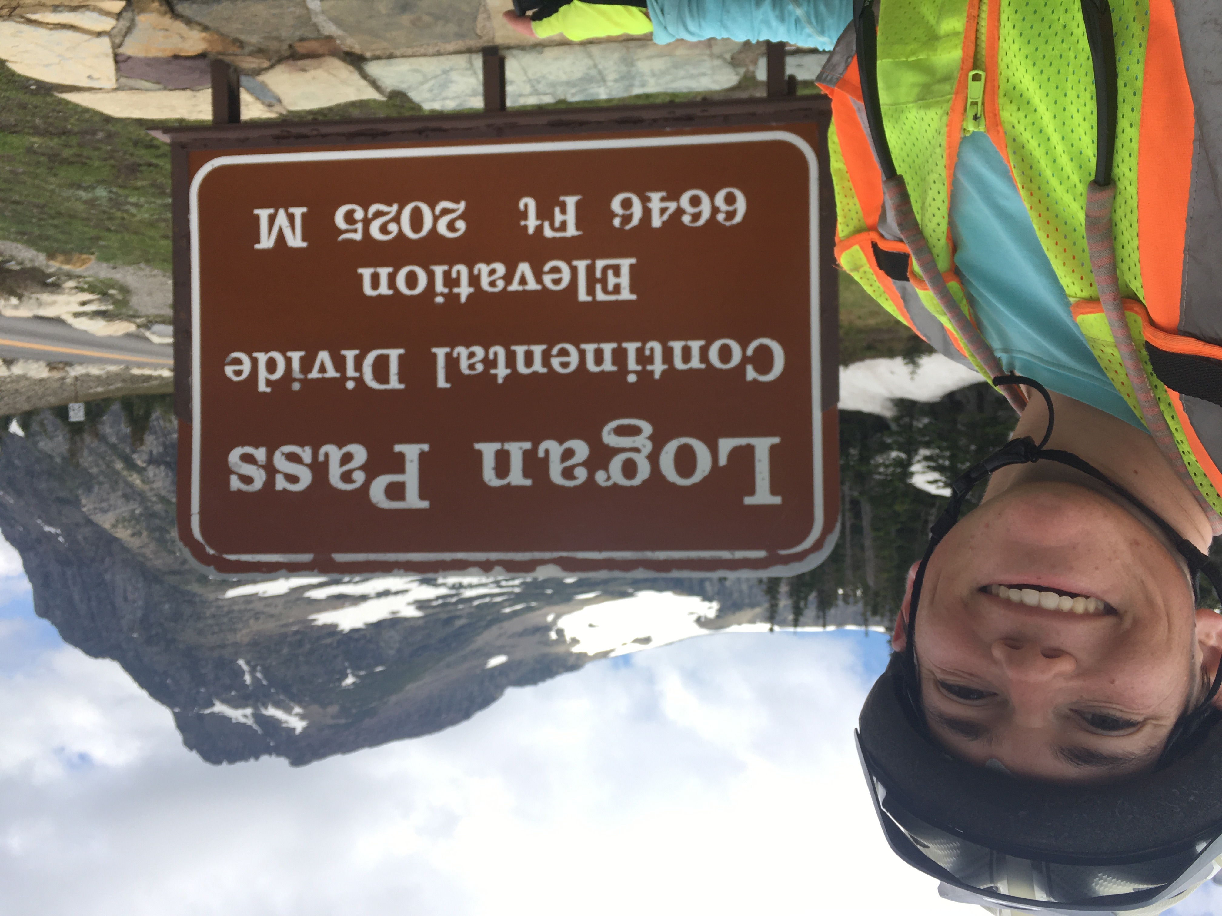 Zeph takse a selfie in front
of a sign reading 'Logan Pass Continental Divide Elevation 6646 Ft 2025 M'.
In the background is a rugged peak with some snow on the left side.