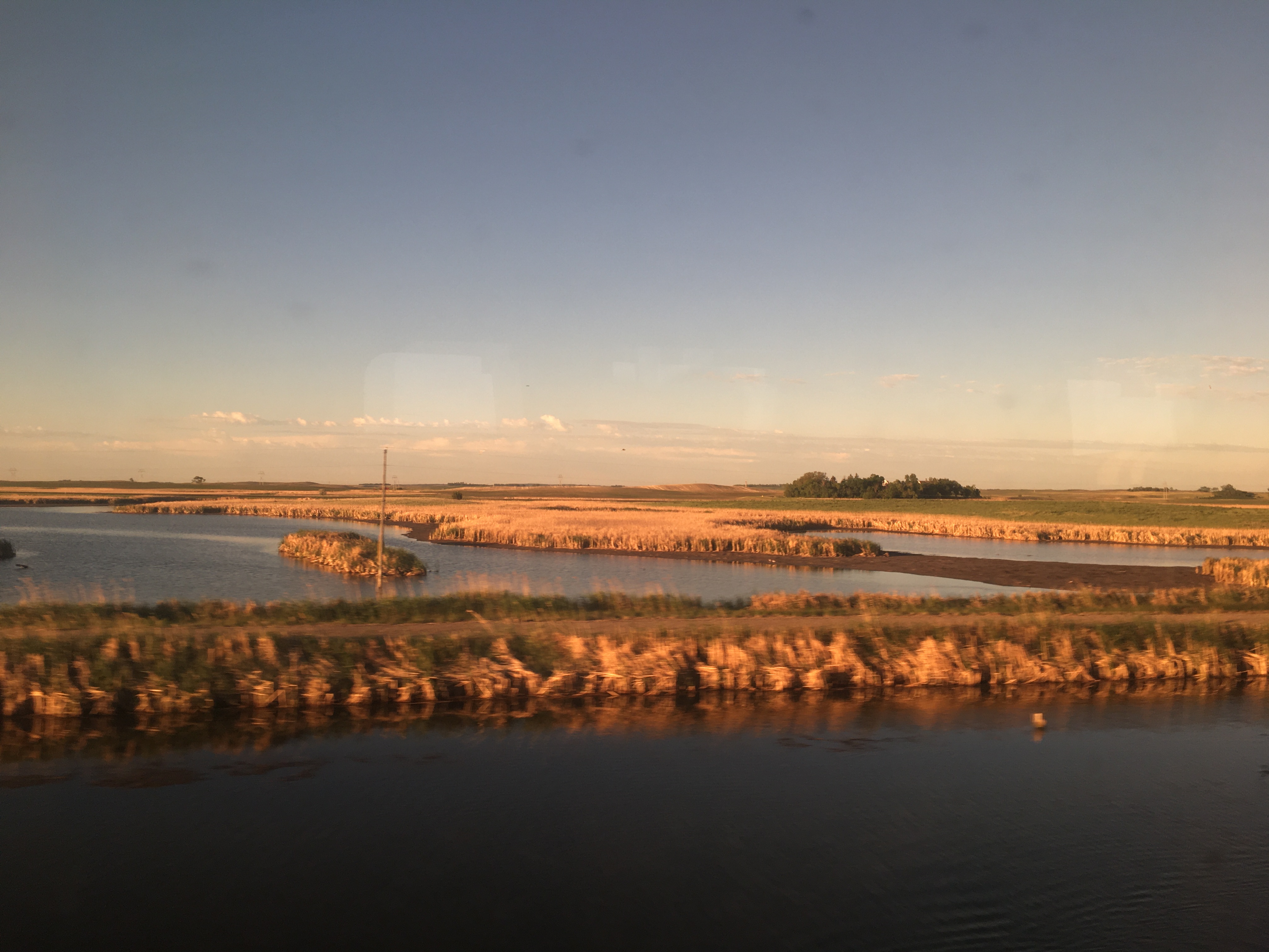 Meandering water features with
grassy berms and islands, and a field in the background. Gentle clouds on
the horizon, with a single patch of trees.