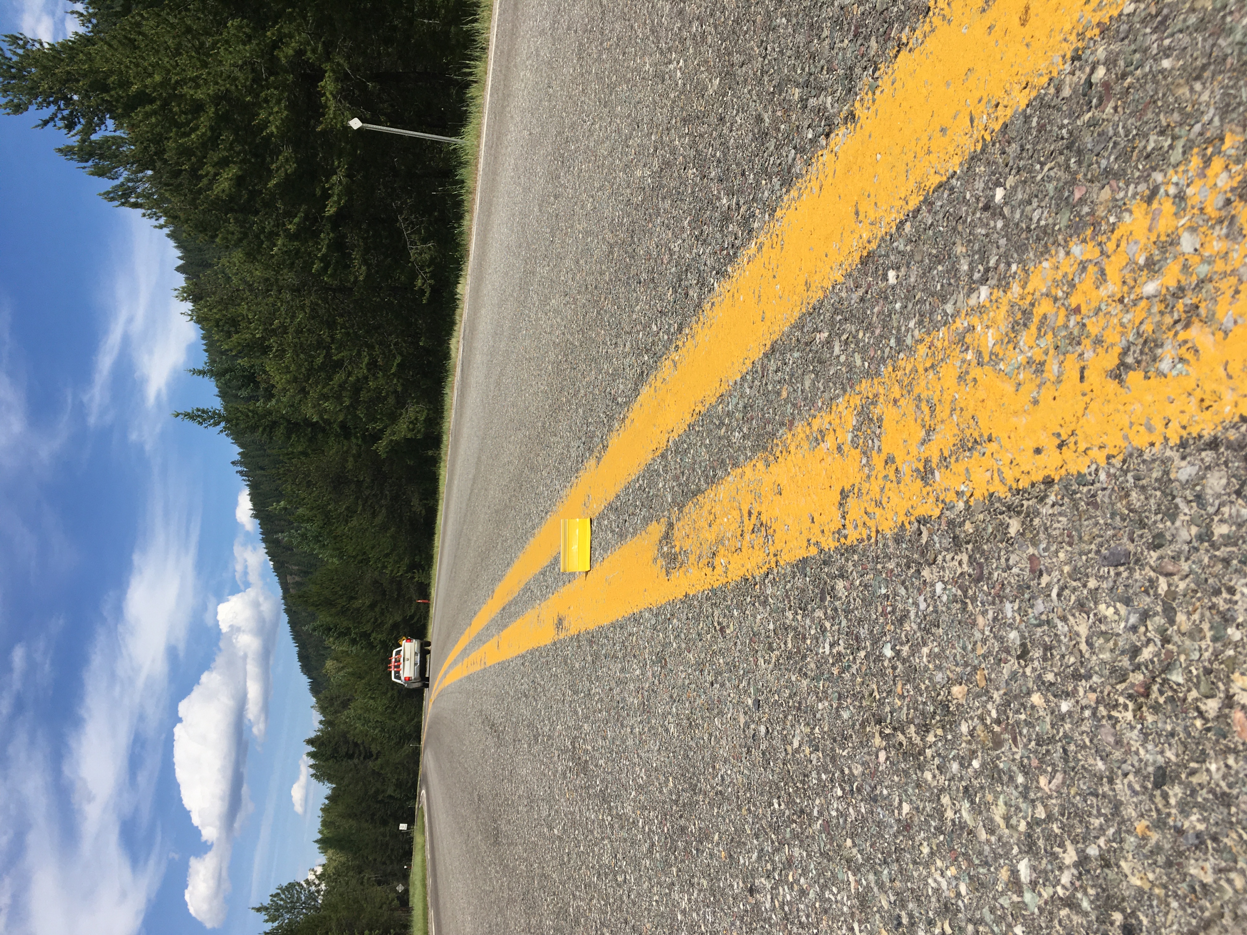 A picture taken from road
level shows a double yellow line and one sticking-up reflector. There's a
road maintenance vehicle departing in the backgrounnd, and trees on the
right side of the road.